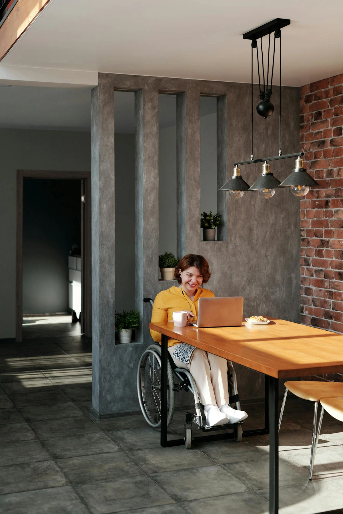 Eine Frau mit einer Behinderung. Sie sitzt im Rollstuhl in einem Kaffeehaus und sieht sich gerade etwas auf einem Laptop an. Sie wirkt fröhlich.